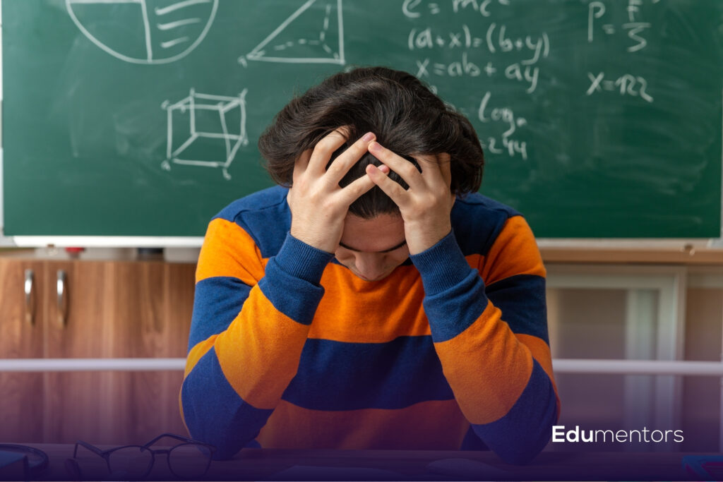 Student holding their head in stress while preparing for GCSE mock exams in a Maths classroom.